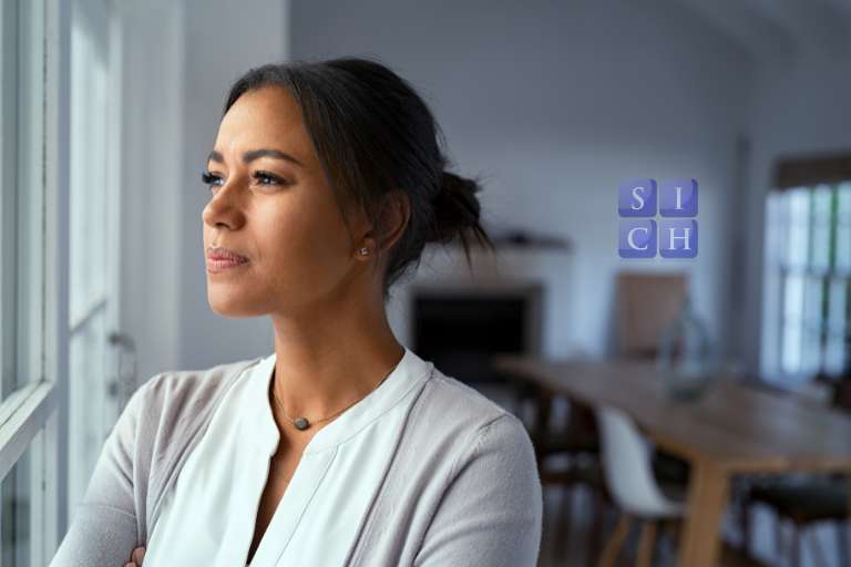 Person looking thoughtfully out of a window, contemplating a career change to hypnotherapy for personal fulfilment and purpose.